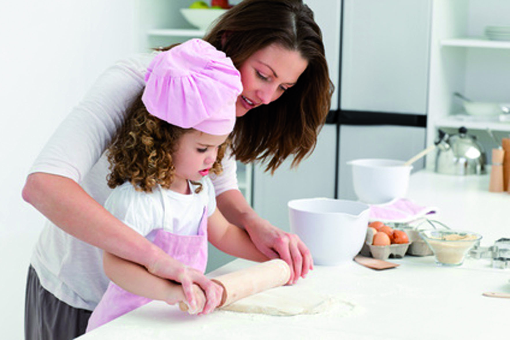Mother and daughter using a rolling pin together in the kitchen